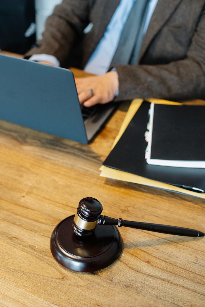 수원변호사 법무법인 From above of crop anonymous male lawyer in formal clothes typing on laptop while sitting at wooden table with stack of documents and gavel