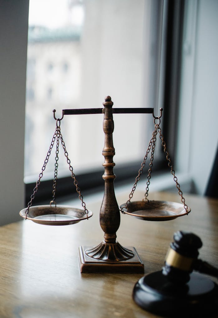 Offerings Decorative judgement scale and gavel placed on desk in light lawyer office against window