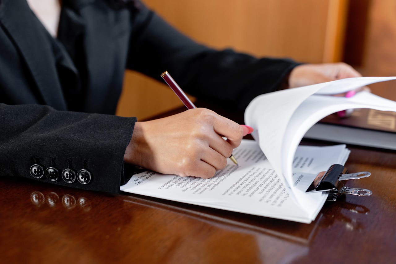 수원변호사 법무법인 Close-up of a woman signing legal documents with a pen in an office setting.